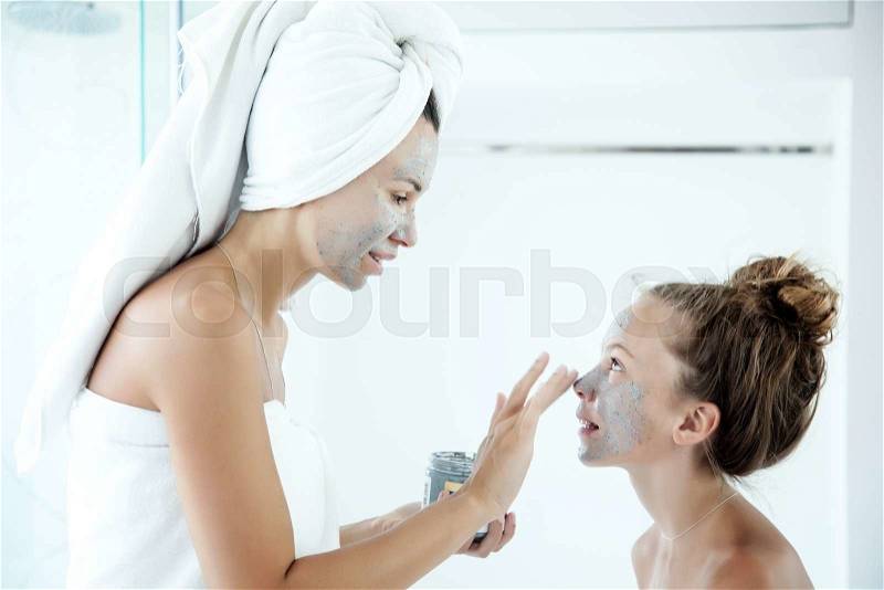 Mother and tween daughter make a clay facial mask, family scin care in the bathroom, stock photo