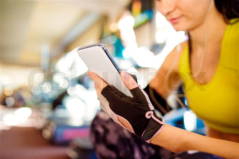 Attractive fit woman in a gym with smart phone against a row of treadmills, stock photo