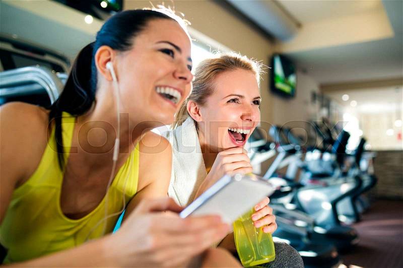 Two attractive fit women in a gym during a break with smart phone laughing, stock photo