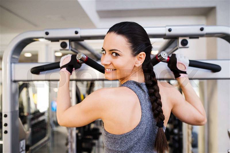 Close up of attractive fit woman flexing back muscles on cable machine, back view, rear viewpoint, stock photo