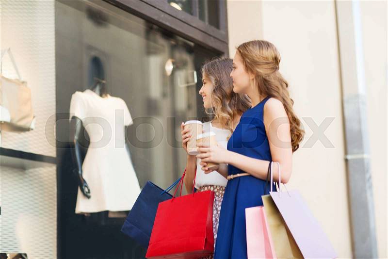 Sale, consumerism and people concept - happy young women with shopping bags and coffee paper cups looking at shop window outdoors, stock photo