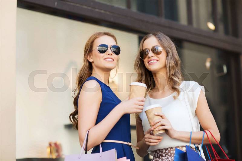 Sale, consumerism and people concept - happy young women with shopping bags and coffee paper cups at shop window in city, stock photo