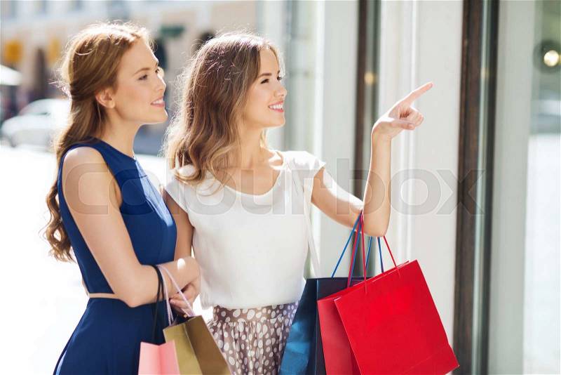 Sale, consumerism and people concept - happy young women with shopping bags pointing finger to shop window in city, stock photo