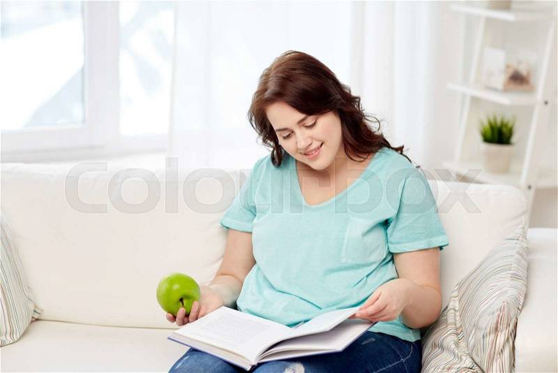 Healthy eating, organic food, fruits, diet and people concept - happy young plus size woman reading book and eating green apple at home, stock photo