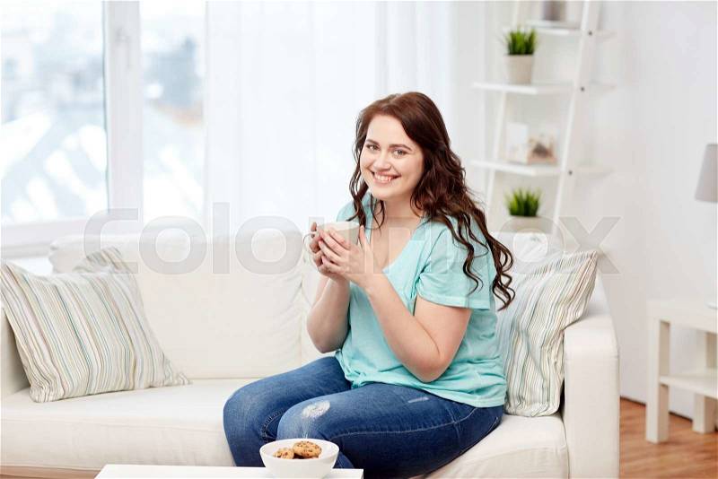 People, food, eating and leisure concept - happy plus size young woman with cup of tea with cookies at home, stock photo