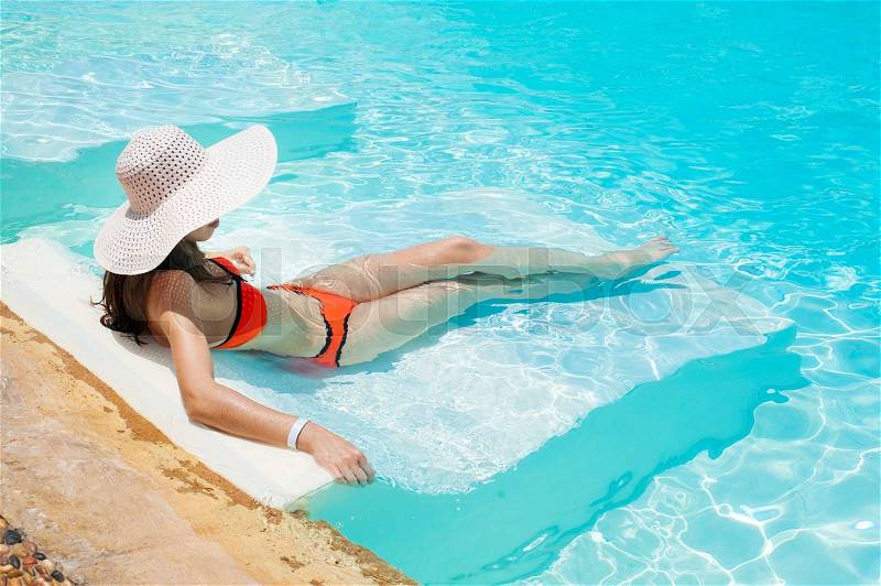 Beautiful woman in a white hat and bikini lying in a pool, stock photo