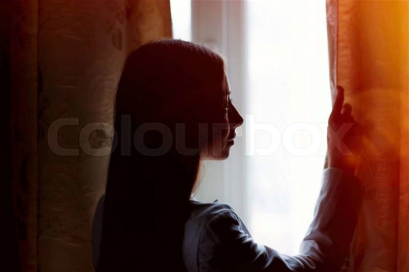 Beautiful young woman standing near a window in the room, stock photo