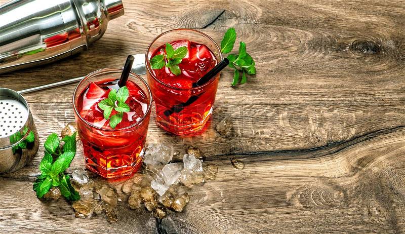 Red cocktail with ice, mint leaves and strawberry on wooden background, stock photo