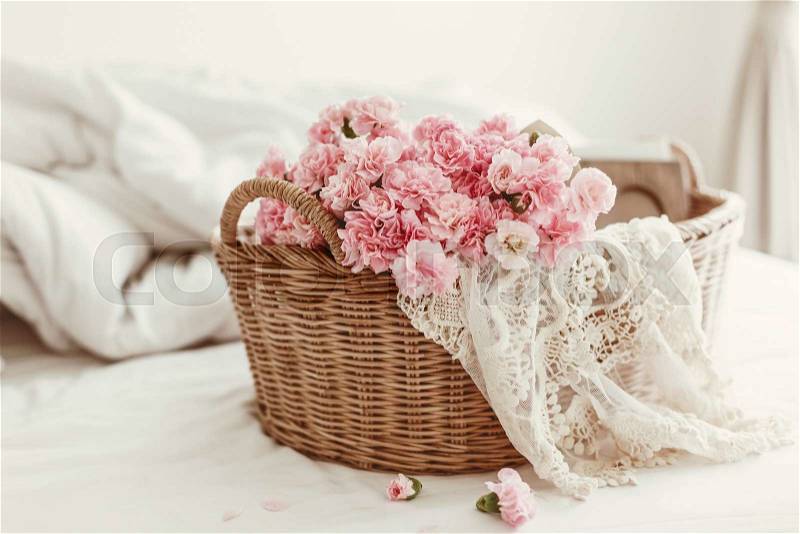 Shabby chic style. Pink pastel flowers in wicker basket on the bed, stock photo