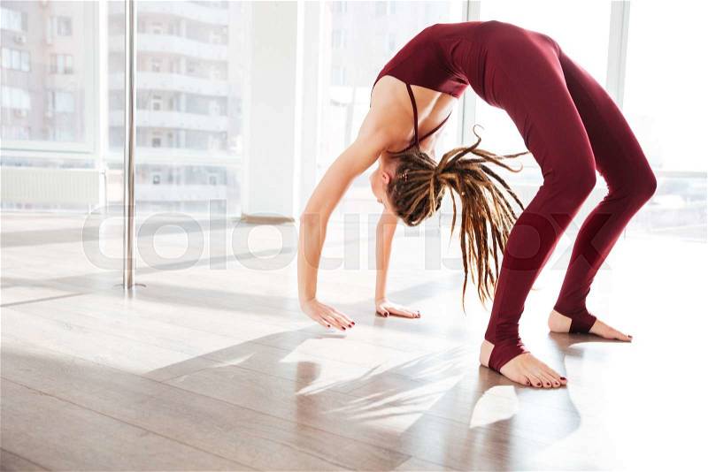 Beautiful young woman with dreadlocks bending and doing yoga in studio, stock photo