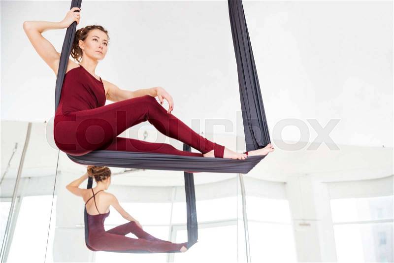 Serious attractive young woman doing antigravity yoga in studio, stock photo