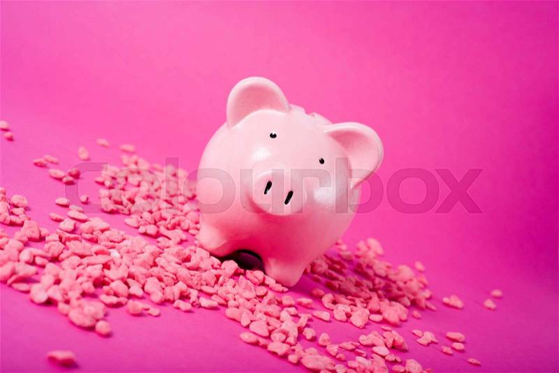 Piggy bank on magenta colored background, with pink gravel, tilted view, stock photo