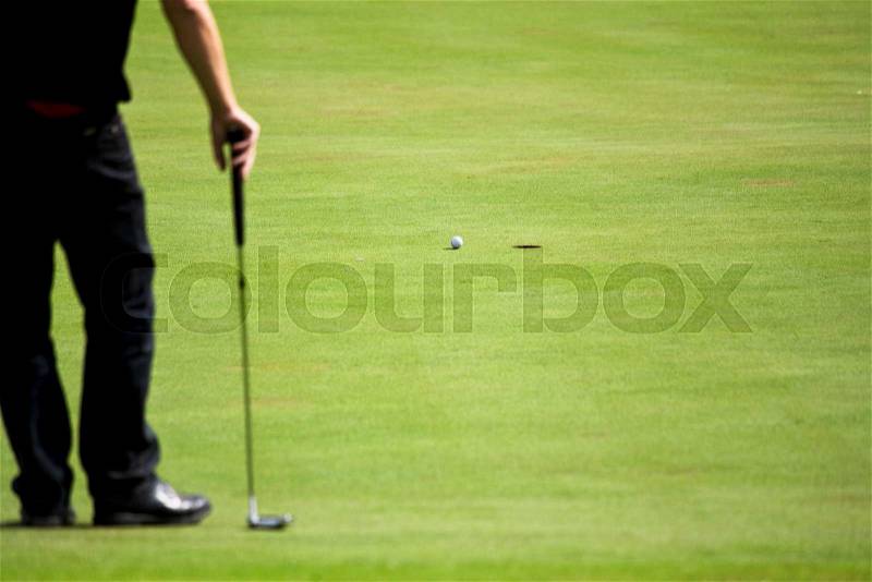 Golf player standing on the green watching his ball run to the hole, focus on the ball, stock photo
