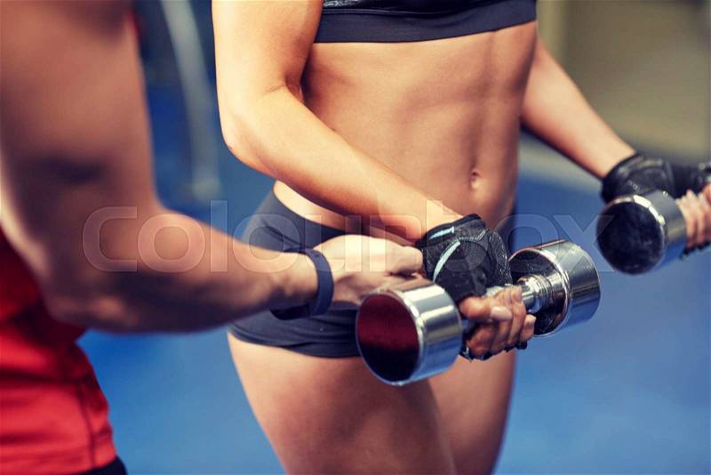 Fitness, sport, bodybuilding and weightlifting concept - close up of young woman and personal trainer with dumbbells flexing muscles in gym, stock photo