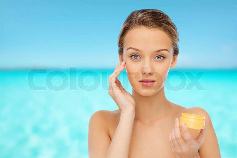 Beauty, people, cosmetics, skincare and cosmetics concept - young woman applying cream to her face, stock photo