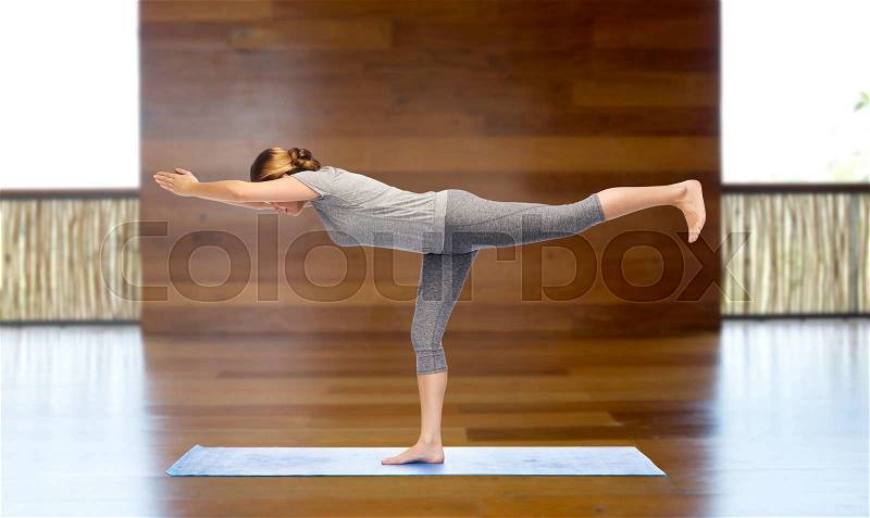 Fitness, sport, people and healthy lifestyle concept - woman making yoga warrior pose on mat over wooden gym background, stock photo