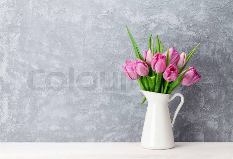 Fresh pink tulip flowers bouquet on shelf in front of stone wall. View with copy space, stock photo