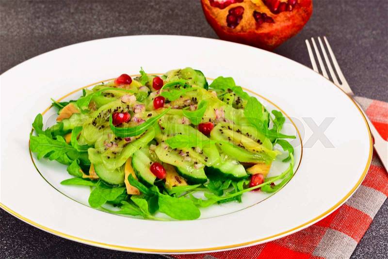 Healthy and diet food: Salad with arugula, avocado, kiwi, cucumber, onion, pomegranate on White Plate Studio Photo, stock photo