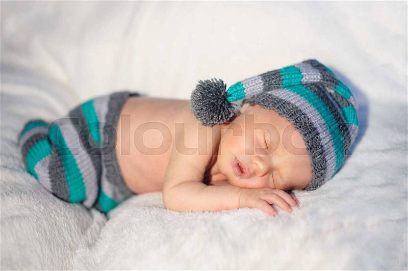 Little baby boy in knitted hat lying on the bed, stock photo