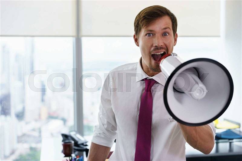 Young executive office worker holding megaphone and speaking at camera with confidence and funny expression. Copy space, stock photo
