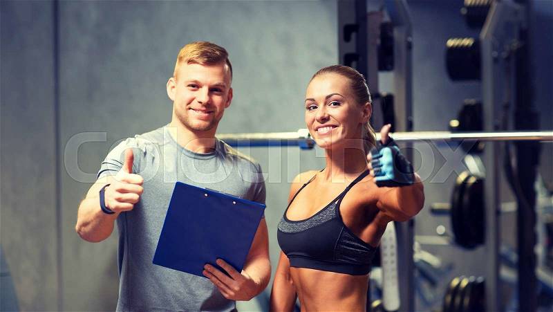 Fitness, sport, exercising and diet concept - smiling young woman and personal trainer with clipboard showing thumbs up in gym, stock photo