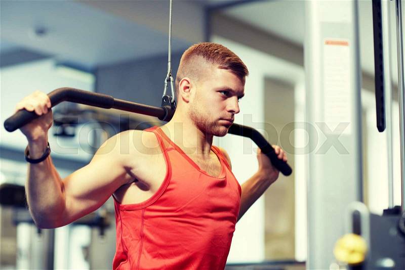 Sport, fitness, bodybuilding, lifestyle and people concept - man exercising and flexing muscles on cable machine in gym, stock photo