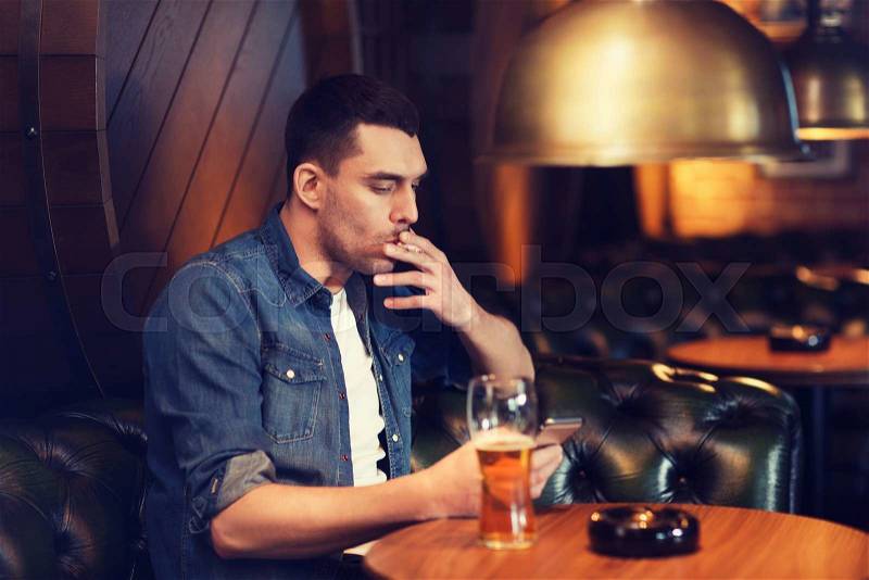 People and bad habits concept - man drinking beer and smoking cigarette at bar or pub, stock photo