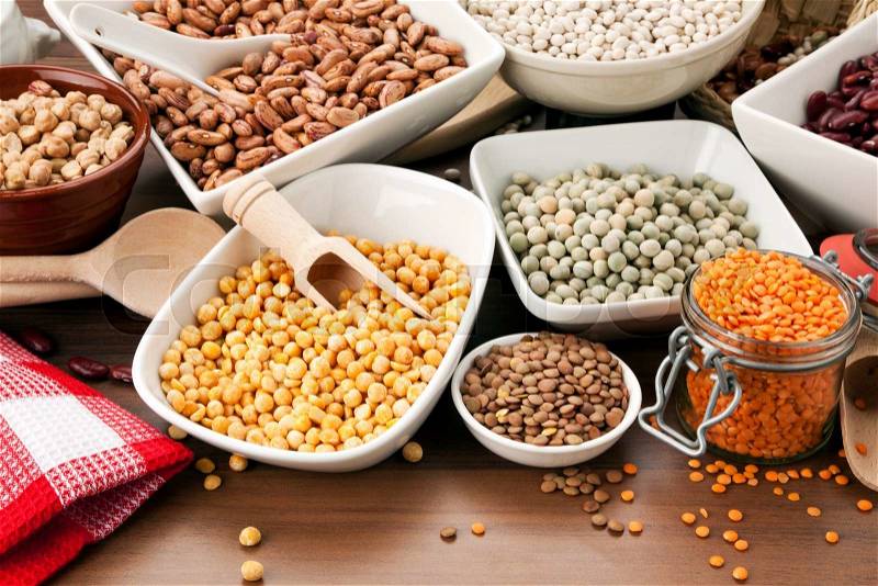 Variety of legumes in bowls and glasses, arranged on kitchen table, stock photo