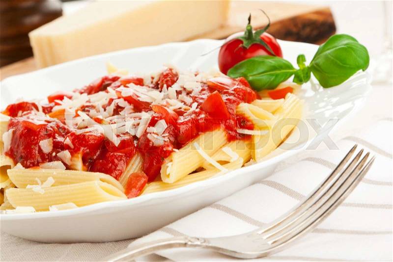 Penne with tomato sauce and grated cheese, garnished with tomato and basil leaves, tilted view, stock photo