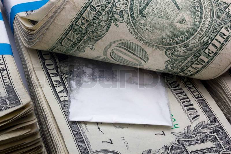 Small sealed bag with drugs laying in a stack of cash, stock photo