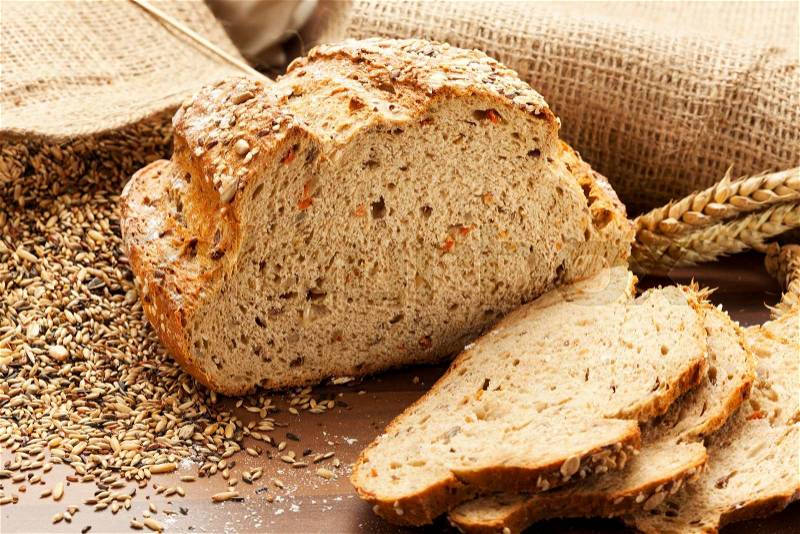 Whole grain bread with slices, burlap bags with grain in background, stock photo