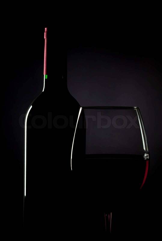 Bottle and glass of red wine in low light, stock photo