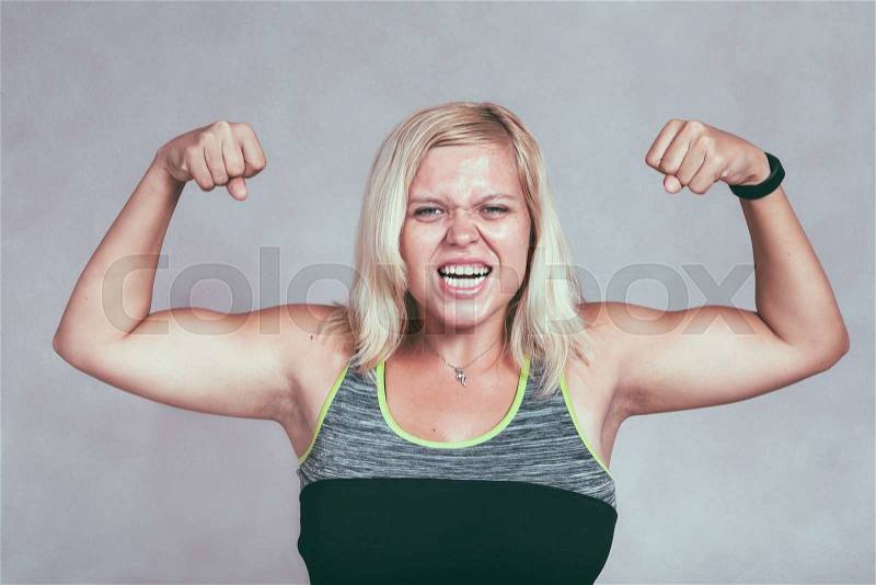 Strong excited muscular woman flexing her muscles. Young blond sporty female showing arms and biceps, stock photo