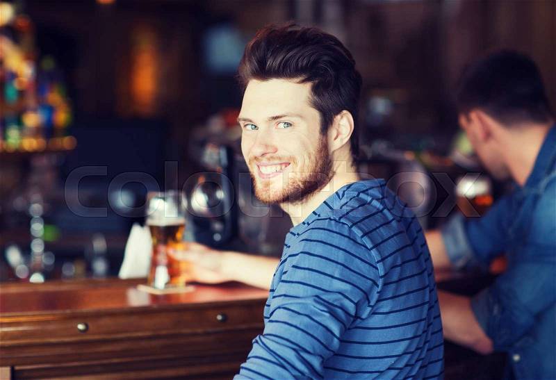 People, leisure and drinks concept - happy young man drinking beer at bar or pub, stock photo