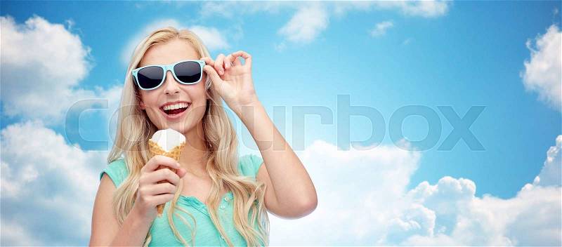 Summer, junk food and people concept - young woman or teenage girl in sunglasses eating ice cream over blue sky and clouds background, stock photo
