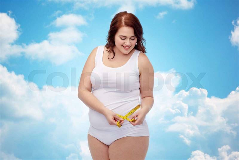 Weight loss, diet, slimming, size and people concept - happy young plus size woman in underwear measuring tape over blue sky and clouds background, stock photo