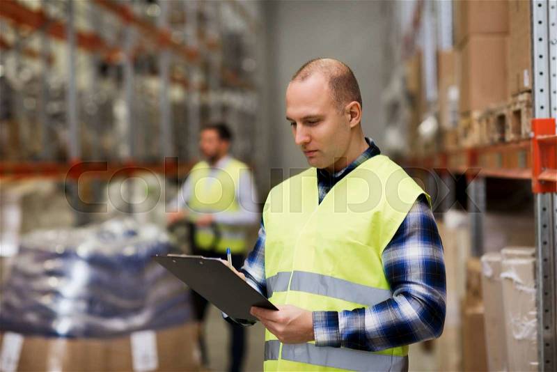 Wholesale, logistic, people and export concept - man with clipboard in reflective safety vest at warehouse, stock photo