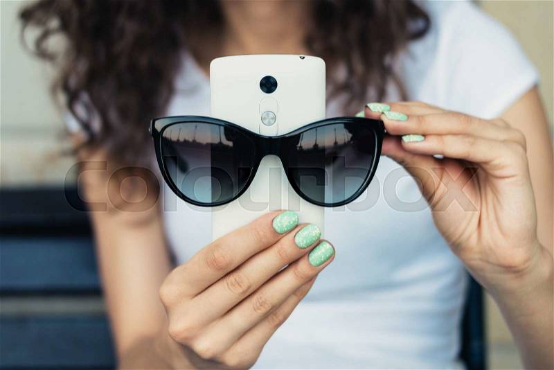 Girl in white t-shirt holding a mobile phone and sunglasses closeup, stock photo