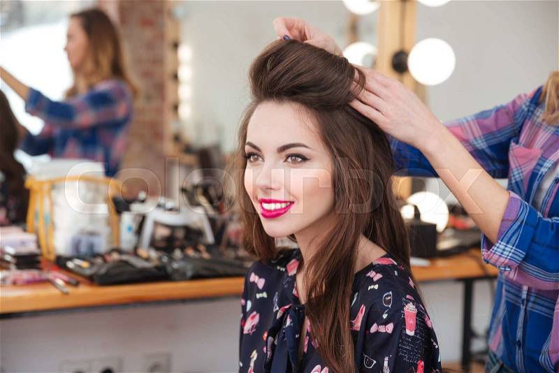 Professional female hairdresser making hairstyle to cheerful young woman with long hair, stock photo