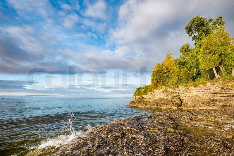 A small wave breaks and splashes under a cloudy blue sky at Door County, Wisconsin\'s Cave Point on the coast of Lake Michigan, stock photo