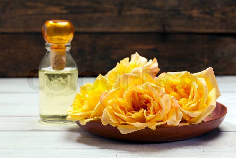 Yellow rose blossoms in wooden bowl, fragrance bottle in back, stock photo