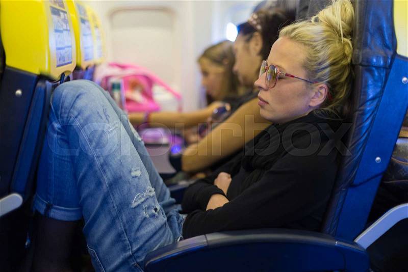 People flying by plane. Interior of airplane with passengers sleeping on seats. Tired woman napping on uncomfortable seat on airplane. Commercial transportation by planes, stock photo