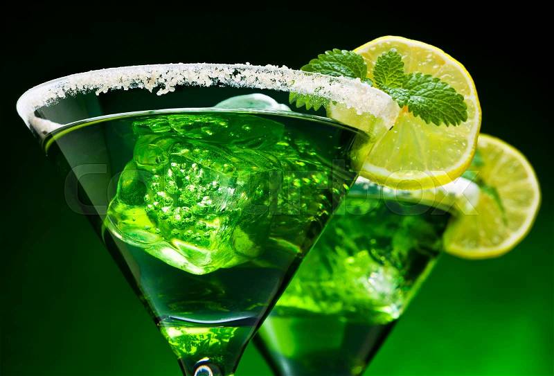 Closeup of green cocktails in martini glasses with ice cubes, lime slices, mint leaves and sugared edge, stock photo