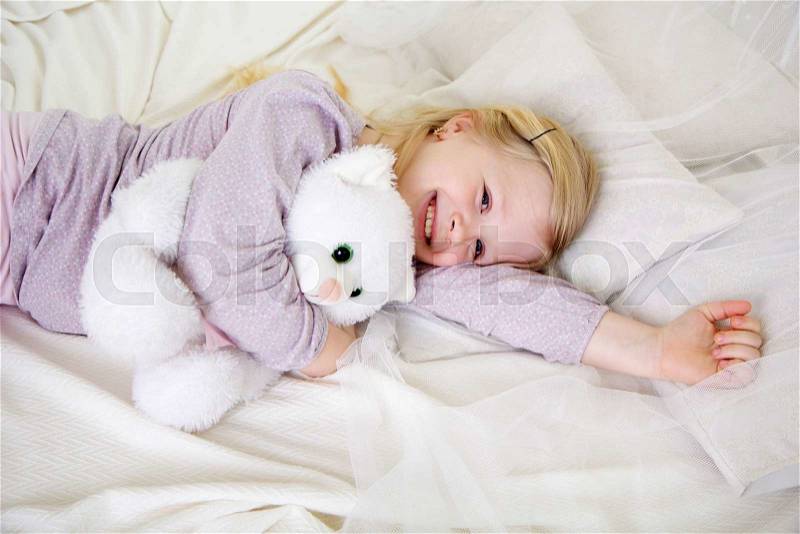 Happy smiling girl is holding her teddy bear in the bed, good night, stock photo