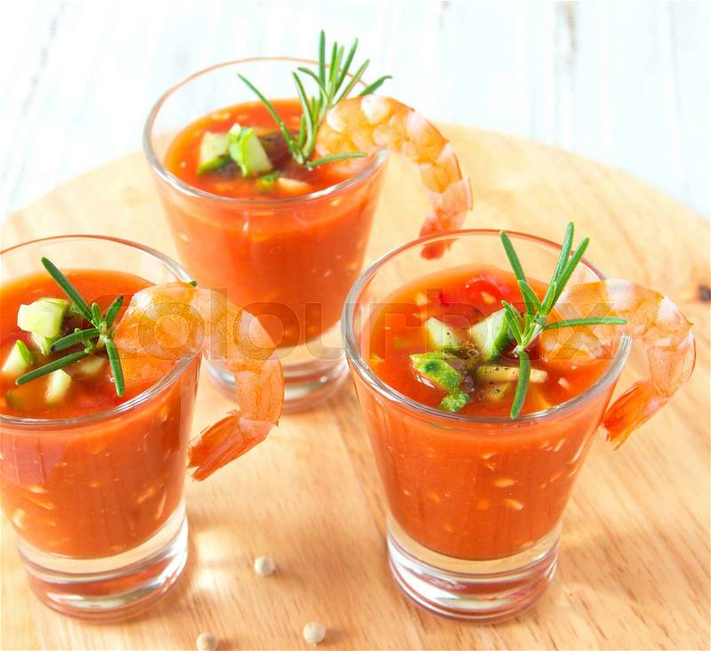 Tasty delicious fresh cold vegetable tomato soup with shrimps and rosemary in portion glasses on wooden board close up, horizontal. Party appetizer, stock photo