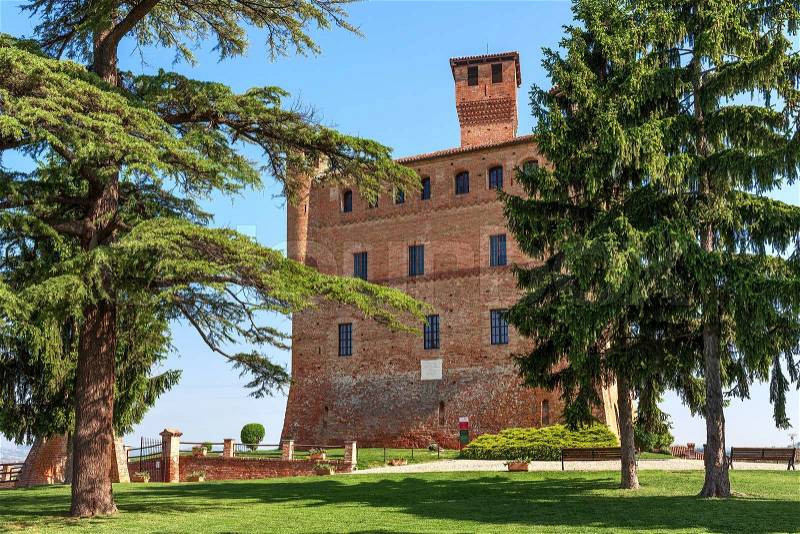 Small green lawn, trees and medieval castle in Piedmont, Northern Italy, stock photo