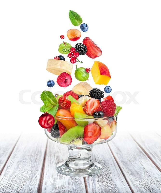 Fruit salad in a glass bowl with ingredients flying in the air on white wooden table\\ , stock photo