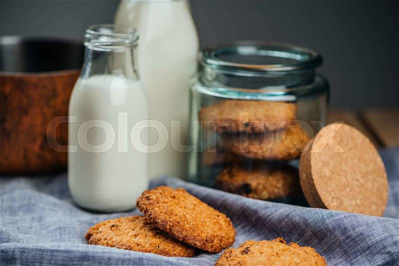 Oatmeal cookies in glass jar and milk in bottles on the table, stock photo