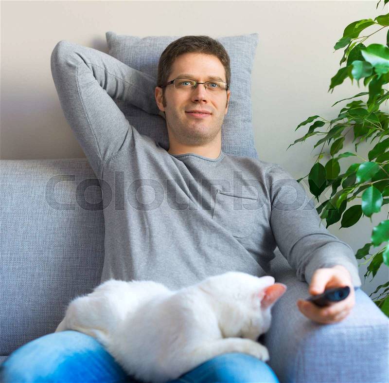 Man relaxing on the sofa with tv remote control. Watching TV with his cat, stock photo
