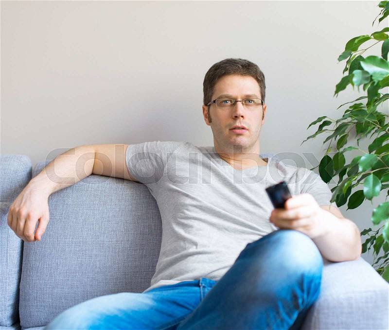 Man relaxing on the sofa with tv remote control. Place for text, stock photo